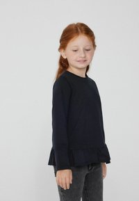 Černé dlouhé rukávy tričko s volánkovým lemem, vyrobené z měkké tkaniny. Jednoduchý design, kulatý výstřih a volný střih.