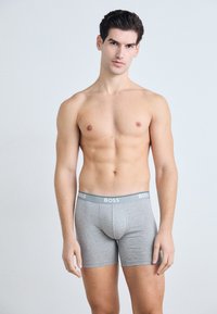 Graue Baumwollboxershorts mit körperbetontem Design, ausgestattet mit einem weichen grauen Bund, der mit "BOSS" in Weiß bedruckt ist. Schlichte und glatte Textur.