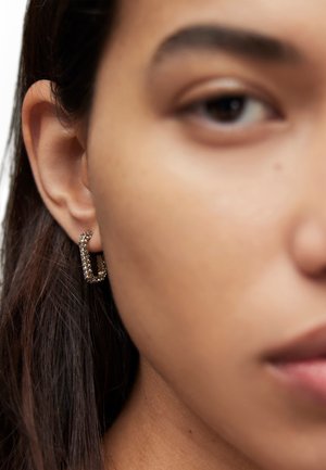 Goldene Creolen mit rechteckigem Design, verziert mit kleinen klaren Kristallen entlang der Kanten, die im Ohr eines Models präsentiert werden.