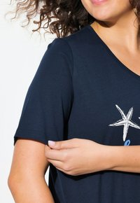 T-shirt blu navy a maniche corte con una grafica di una stella marina bianca. Realizzato in tessuto morbido con scollatura a V e una vestibilità comoda.
