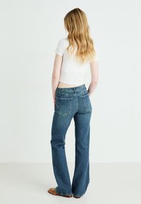 Jeans blu a vita alta e a zampa d'elefante in denim; cinque tasche con cuciture visibili; indossati con una t-shirt bianca cropped.