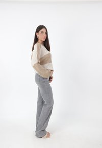 Beige en crèmekleurige gestreepte trui van breiwerk met lange mouwen, gecombineerd met hoge grijze jeans en lichte sandalen. Neutrale kleurenpalet.