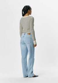 Stribet langærmet bluse i cremefarvet og marineblå, parret med lyseblå højtaljede jeans. Tætsiddende sweater med ribbede manchetter. Flade sorte sko.