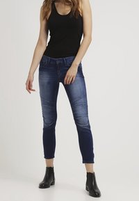 Jeans i denim med en mörkblå gradient och urblekta accenter. Har sömnad vid knäna och en slim fit. Kombineras med en svart linne och ankelskor.