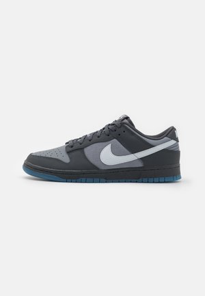 Niskie buty sportowe Nike w ciemnym i jasnym odcieniu szarości z białym logo Swoosh oraz niebieskawą gumową podeszwą, widoczne z boku.