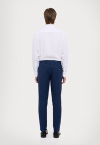 Vit långärmad skjorta med knäppta ärmslut, kombinerad med marinblå skräddarsydda byxor. Outfiten har en enfärgad textur och en klassisk passform.