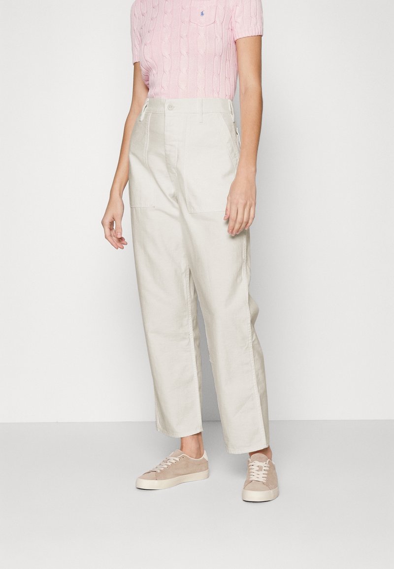 Ljust beiga vida byxor med två framfickor och hög midja. Matchat med en rosa kabelstickad t-shirt med kort ärm och beiga sneakers.