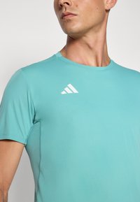 Short-sleeve athletic shirt in light blue, made from stretchy material, featuring a small white logo and seamless design along the neckline.