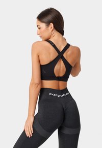 Melnā sporta krūšturis ar krustveida siksnām un izgriezumu detaļām, apvienots ar augsto vidukli, tumši pelēkām legingām ar teksturētām akcentiem.