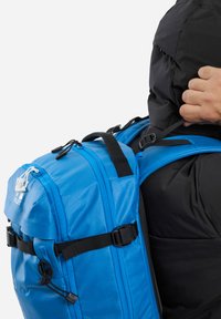 Sac à dos bleu avec une surface texturée, doté de sangles et d'accents noirs. Comprend une poignée supérieure, des boucles latérales réglables et des fermetures à cordon.