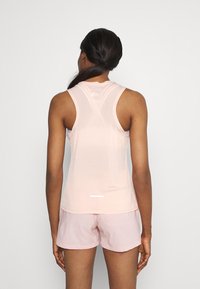 Světle růžový sportovní top s designem racerback, s malým logem na horní části zad a reflexním prvkem podél lemu.