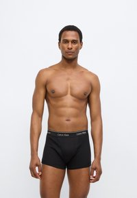 Μαύρα βαμβακερά boxer briefs με απαλό λάστιχο μέσης που φέρει το λογότυπο "Calvin Klein". Το μοντέλο τα φορά, αναδεικνύοντας την εφαρμοστή σχεδίαση και την ομαλή υφή.