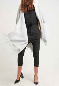 Šedý vlněný šál s třásněmi v okrajích, kombinovaný s černými vysokými zkrácenými kalhotami a černými lodičkami se špičatou špičkou.