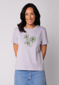 Lila katoenen t-shirt met een groene illustratie van drie klavertjes op de voorkant, met een klassieke ronde hals en korte mouwen.