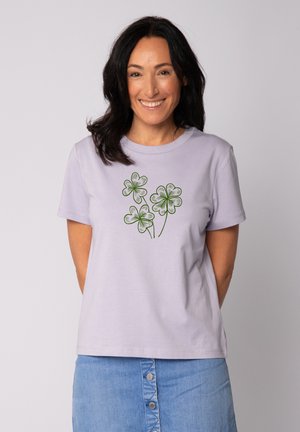 Lilafarbene Baumwoll-T-Shirt mit einer grünen Abbildung von drei Kleeblättern auf der Vorderseite, klassischem Rundhalsausschnitt und kurzen Ärmeln.