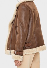 Giacca in shearling marrone con fodera color crema, zip argentata e fascette in pelle marrone regolabili sui polsini, caratterizzata da una finitura testurizzata.