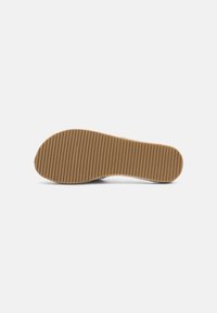 Shoe sole in tan rubber with a horizontal ridged pattern, designed for grip and durability. Smooth edges and a curved toe section.