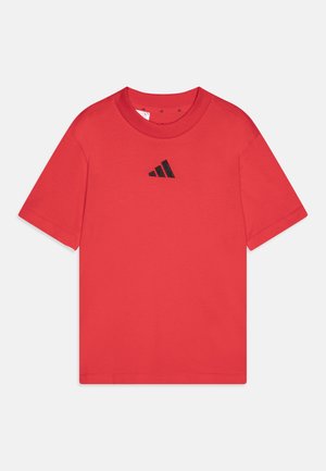 Punane puuvillane T-särk, ümarate krae, lühikeste varrukatega ja väikese musta Adidas logo keskelt rinnal. Sile tekstuur, klassikaline lõige.