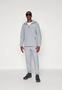 Ljusgrå träningsjacka med huva, dragkedja och sidofickor, matchande byxor och svarta vandringsskor. Solglasögon ingår.