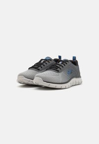 Scarpe da ginnastica grigie con tomaia in rete, lacci neri, dettagli blu e suola testurizzata. Presentano un colletto imbottito e un logo sul lato.