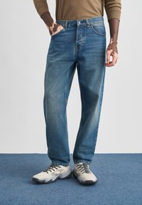 Jasnoniebieskie dżinsy o luźnym kroju, z pięcioma kieszeniami i zapięciem na guzik. Noszone z szaro-czarnymi trampkami.