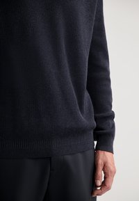 Pulover în nuanță de navy închis, din tricot cu structură ondulată, cu mâneci lungi, având un material texturat și o talie ajustată, asortat cu pantaloni negri.