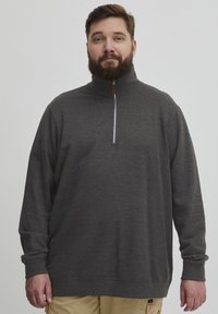 Dunkelgrauer Viertelzip-Pullover mit langen Ärmeln, aus weichem Material gefertigt. Verfügt über einen silbernen Reißverschluss und einen braunen Akzent am Saum.