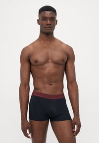 Black boxer briefs with a burgundy waistband featuring embossed branding. The fabric appears smooth, fitted, and stretchable.