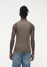 Olijfgroene geribbelde tanktop met een ronde hals, een aansluitend ontwerp en een subtiel logodetail op de achterkant. Gecombineerd met lichtblauwe spijkerbroek.