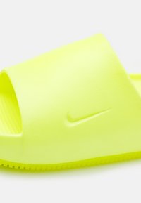 Sandalījums spilgtā dzeltenā krāsā, izgatavots no teksturēta gumijas. Tam ir plata atvērta purna daļa un izveidota pēdas gulta ar diskrētu Nike logo sānos.