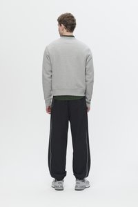 Gray sweatshirt with ribbed cuffs and hem, worn over a green striped shirt, paired with black pants featuring white side stripes. Gray sneakers.