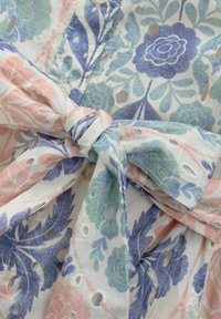Robe en tissu léger avec des motifs floraux en bleu, vert et rose. Comprend des détails décoratifs en œillets et une taille à nouer.