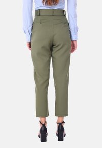 Pantaloni su misura verdi in tessuto liscio, di lunghezza cropped e vita alta. Abbinati a sandali neri con tacco a blocco.
