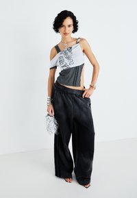 Top gris y blanco asimétrico con estampado gráfico, combinado con pantalones de pierna ancha negros y un bolso plateado brillante. Texturas suaves en todo.