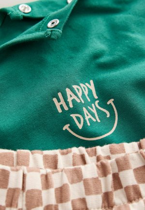 Grünes Baumwolloberteil mit einem lächelnden Gesicht und dem Text "HAPPY DAYS"; ausgestattet mit einem elastischen Gürtel in braun-weißer Karo-Optik.