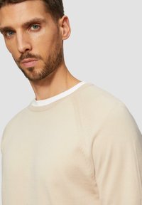 Crème-kleurige pullover trui met een ronde halslijn, geribbelde manchetten en een gladde textuur. Beschikt over een contrasterende witte binnenkraag.