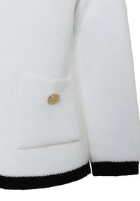 Witte gebreide trui met een voorzak met een gouden knoop, een zwarte geribbelde zoom en een gestructureerde stof. Eenvoudig, klassiek ontwerp.