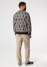 Suéter negro y crema con estampado geométrico, con puños y dobladillo acanalados, combinado con pantalones color topo y zapatillas negras.
