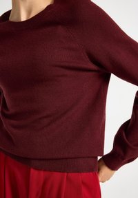 Burgundy neulepaita, jossa on pyöreä pääntie ja ribbikujat, rento istuvuus ja sileä pinta. Yhdistetty punaisen hameen kanssa.