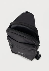 Μαύρη νάιλον τσάντα ώμου με φερμουάρ σε τμήματα, λεία υφή και λογότυπο στο μπροστινό μέρος. Διαθέτει ρυθμιζόμενο ιμάντα για ευκολία στη χρήση.