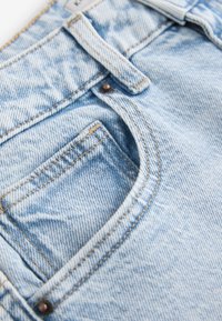 Hellblaue Denim-Jeans in Nahaufnahme mit einer Fronttasche, Gürtelschlaufe und detaillierter Naht.