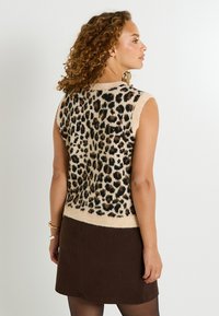 Top sans manches tricoté avec une base beige, présentant un motif léopard en noir et marron, un ourlet côtelé et une coupe légèrement ample.