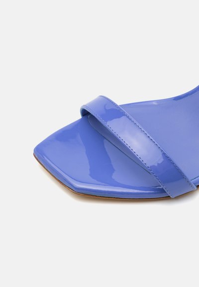 Sandale brillante, bleu clair, avec une semelle plate et une large bride sur le devant. Présente un design de bout géométrique et légèrement pointu.