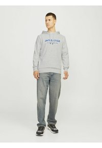 Sudadera gris con texto azul "JACK & JONES" en el frente, combinada con jeans azul claros y zapatillas deportivas negras con suelas blancas.
