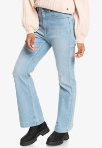 Jeans flare in denim azzurro chiaro con vita alta, caratterizzati da un design pulito e cuciture sottili, abbinati a stivali neri alla caviglia.