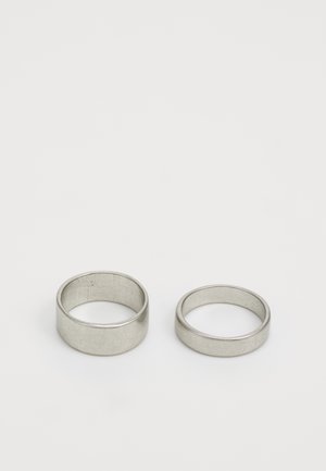 Dva kovinska obroča, en širši in en ožji, oba z gladko, polirano površino in mat srebrno barvo na navadni beli podlagi.