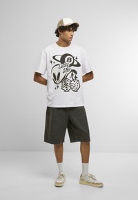 Hvid grafisk t-shirt med sorte motiver af en alien, terninger og en planet. Sammen med mørk denimshorts og beige sneakers.