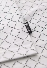 Bavlněná tkanina s bílým pozadím, na kterém se nachází opakující se černý liniový vzor čtverců. Obsahuje malou značkovou látkovou visačku.