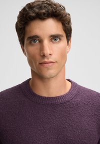 Maglione viola con texture e scollo a costine, realizzato in un tessuto morbido e leggermente peloso. Il design è semplice, senza loghi o motivi visibili.