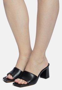 Zwarte leren haksandalen met een vierkante open teenontwerp en een stevige blokhak. Gladde textuur met minimale detailing.